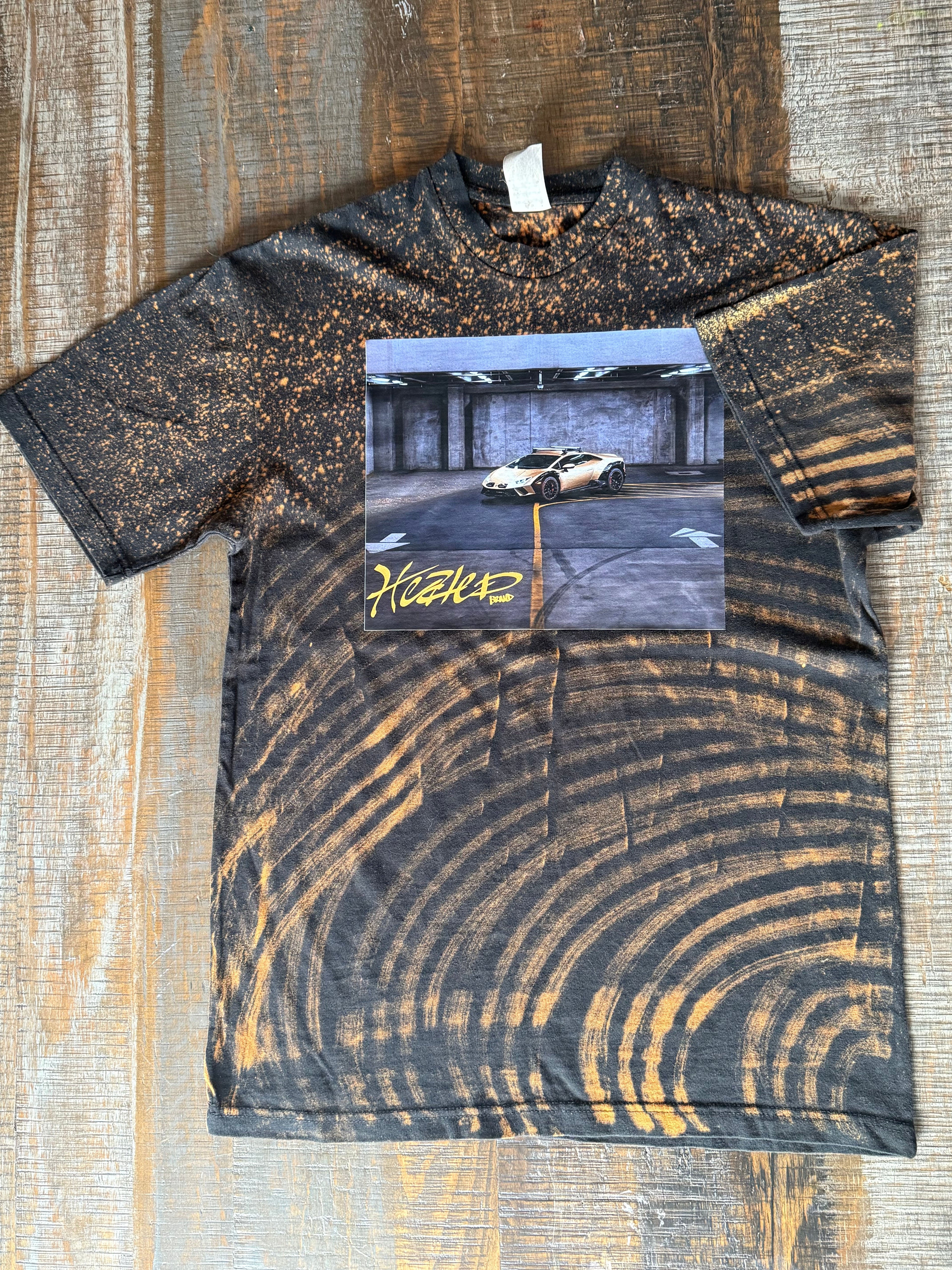 T-shirt with a graphic of a car on a road and 'HUF' logo, displayed on a wooden surface.