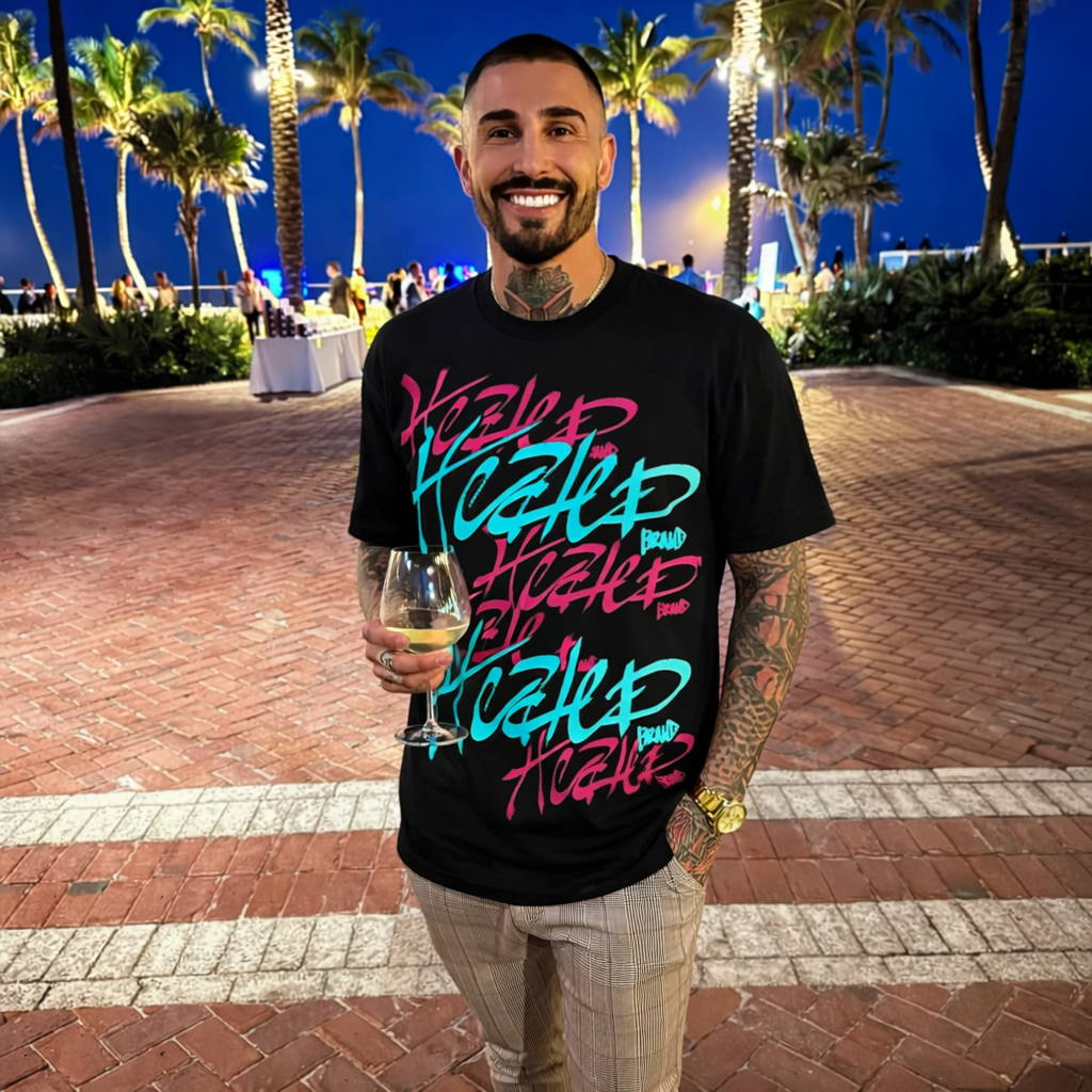 Man wearing a black t-shirt with colorful text, holding a drink, in a tropical outdoor setting at night.